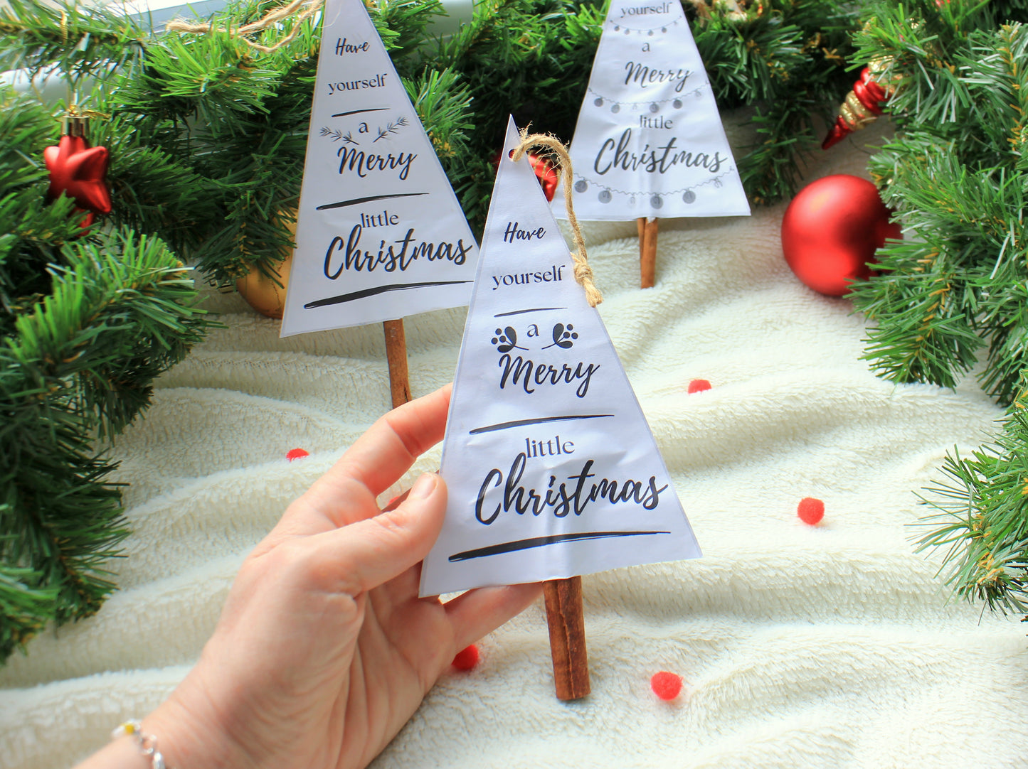 Hand holding a small paper Christmas tree with 'Merry Little Christmas' text by NatkoPatterns