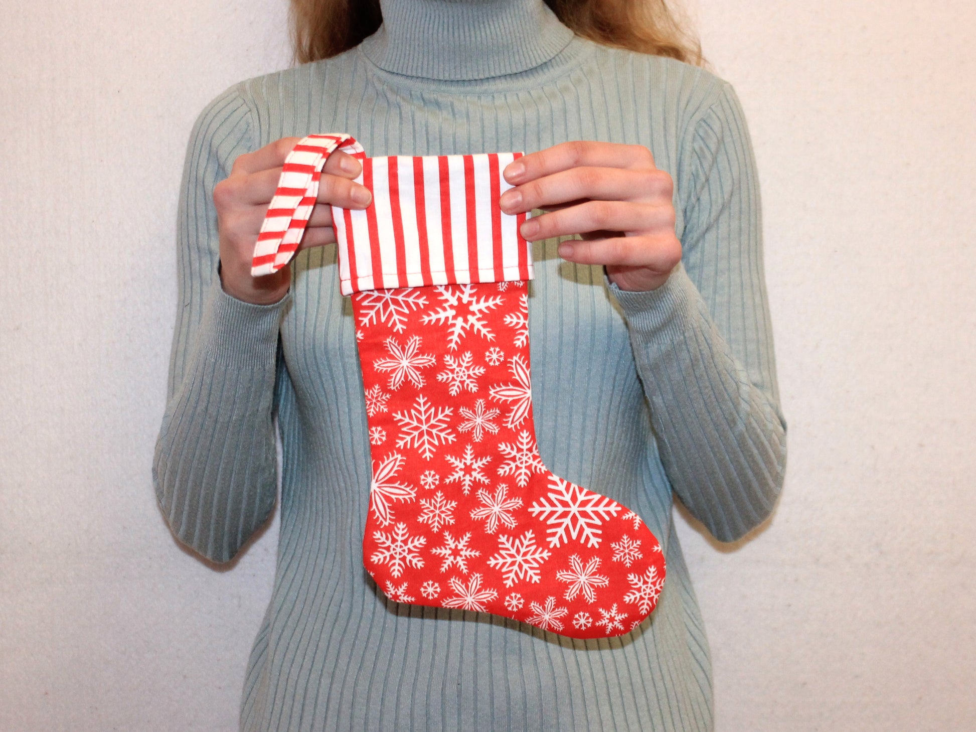 Person holding a red Christmas stocking with white snowflakes and a striped top - easy DIY tutorial by NatkoPatterns