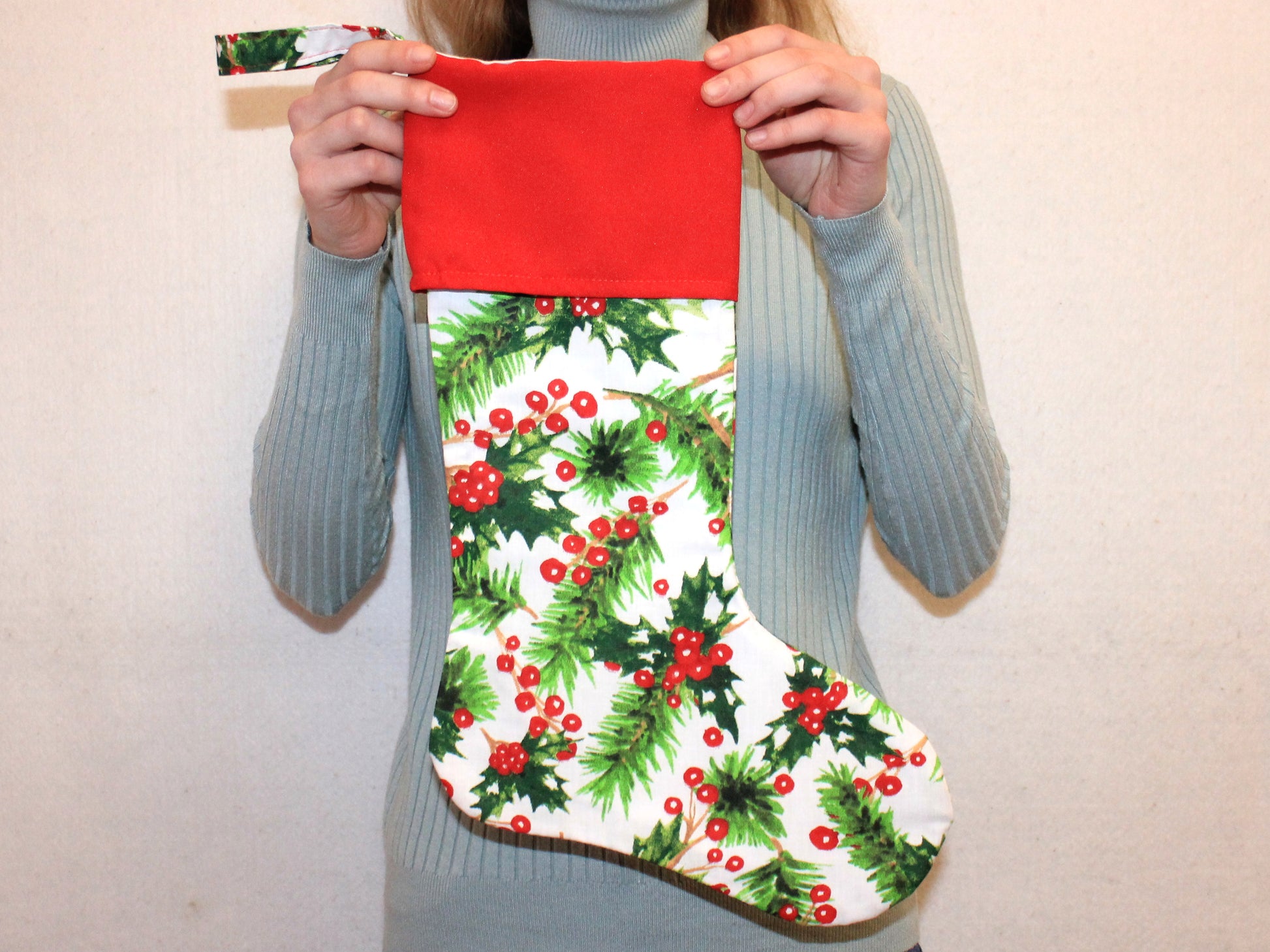 Person holding a Christmas stocking with holly design - sewing pattern PDF by NatkoPatterns