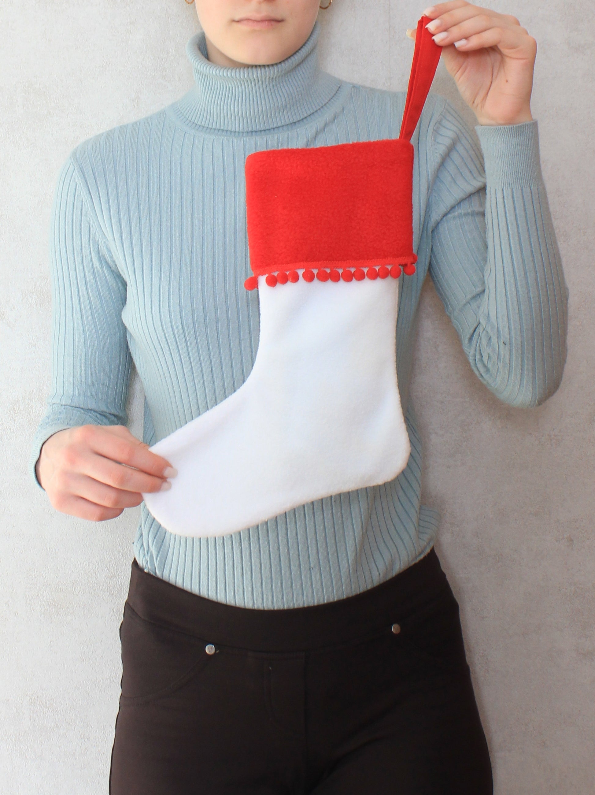 Person holding a white Christmas stocking with red top and pom-pom trim -sewing pattern