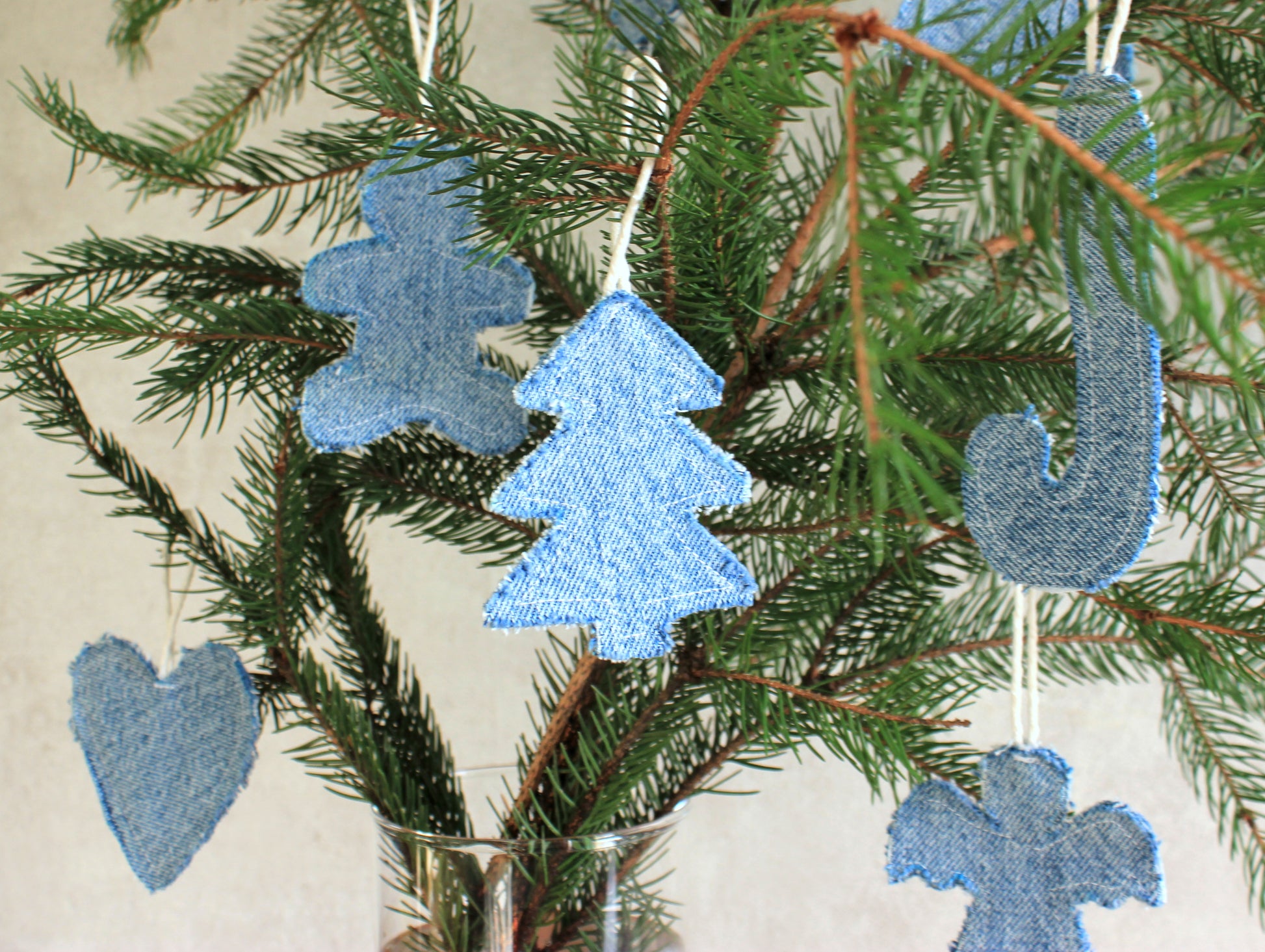 Blue fabric ornaments shaped like trees, hearts, and crosses hanging on a Christmas tree.