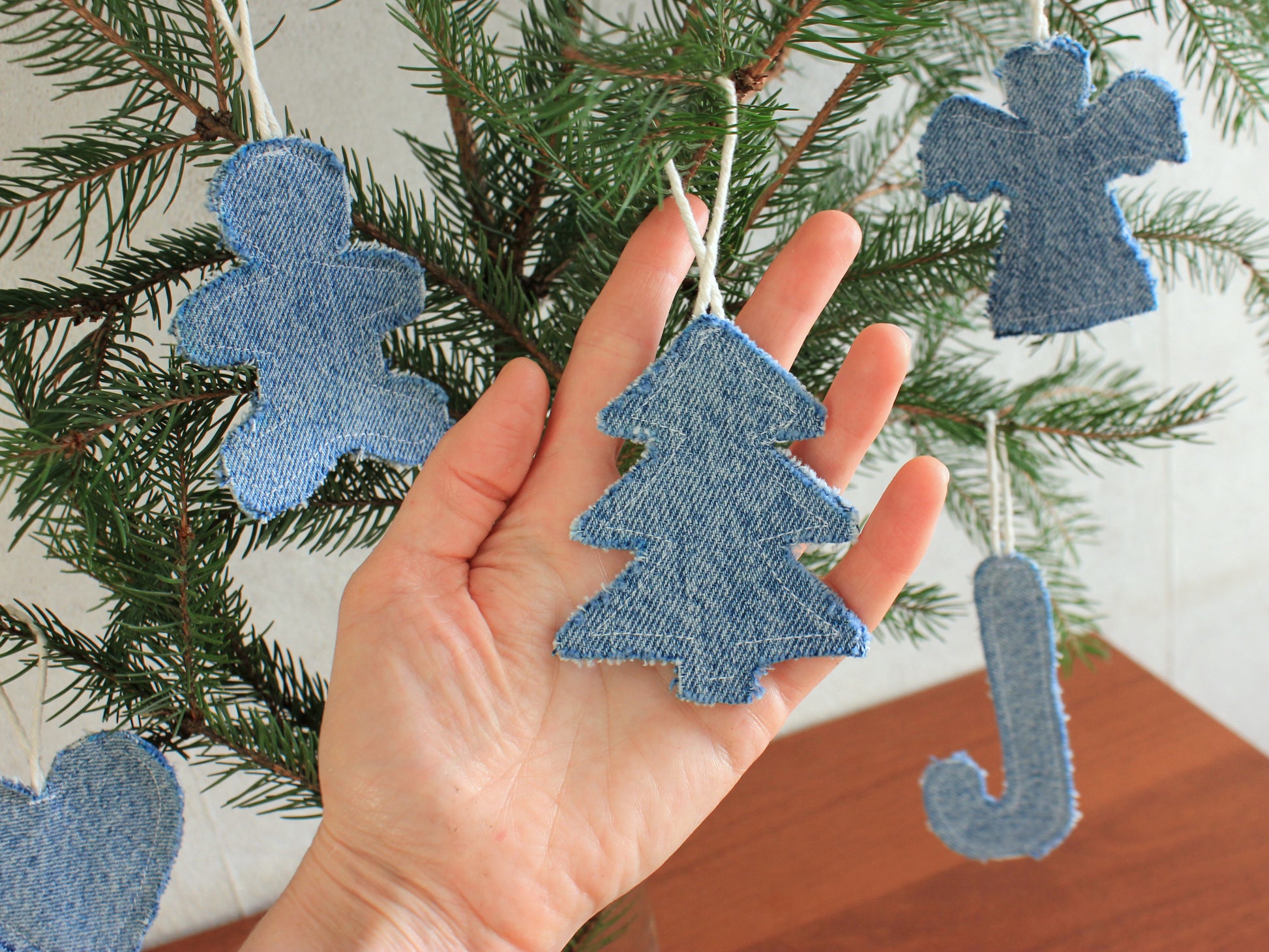 Hand holding denim Christmas tree ornament with more ornaments on a tree - sewing tutorial and templates