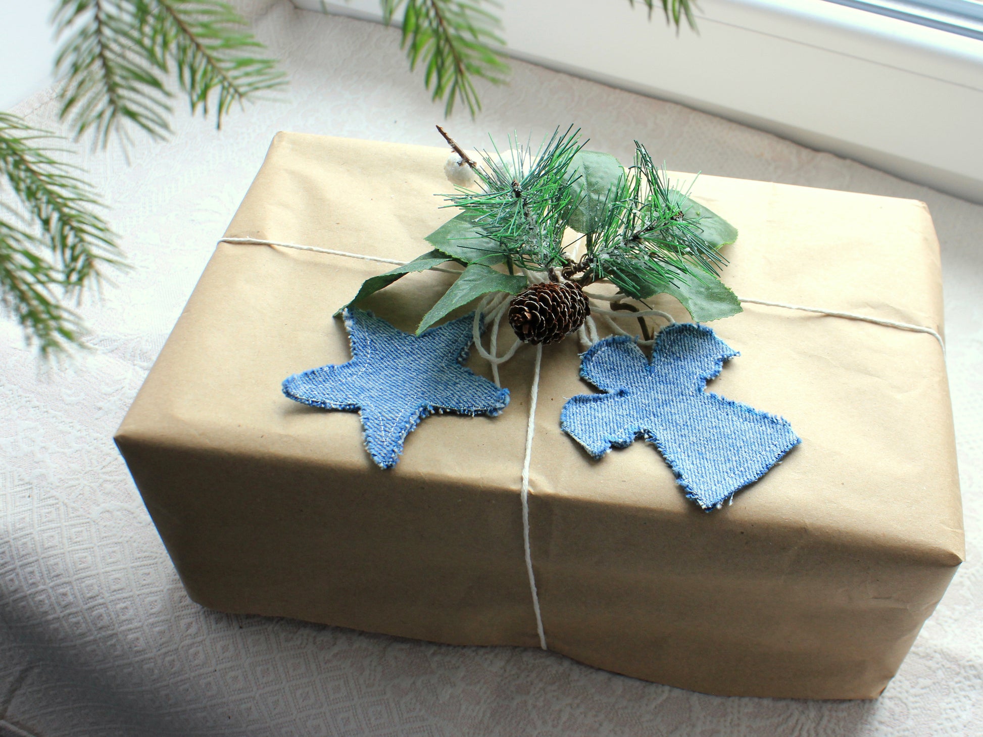 Gift wrapped in brown paper with blue star-shaped decorations and greenery on a light surface.