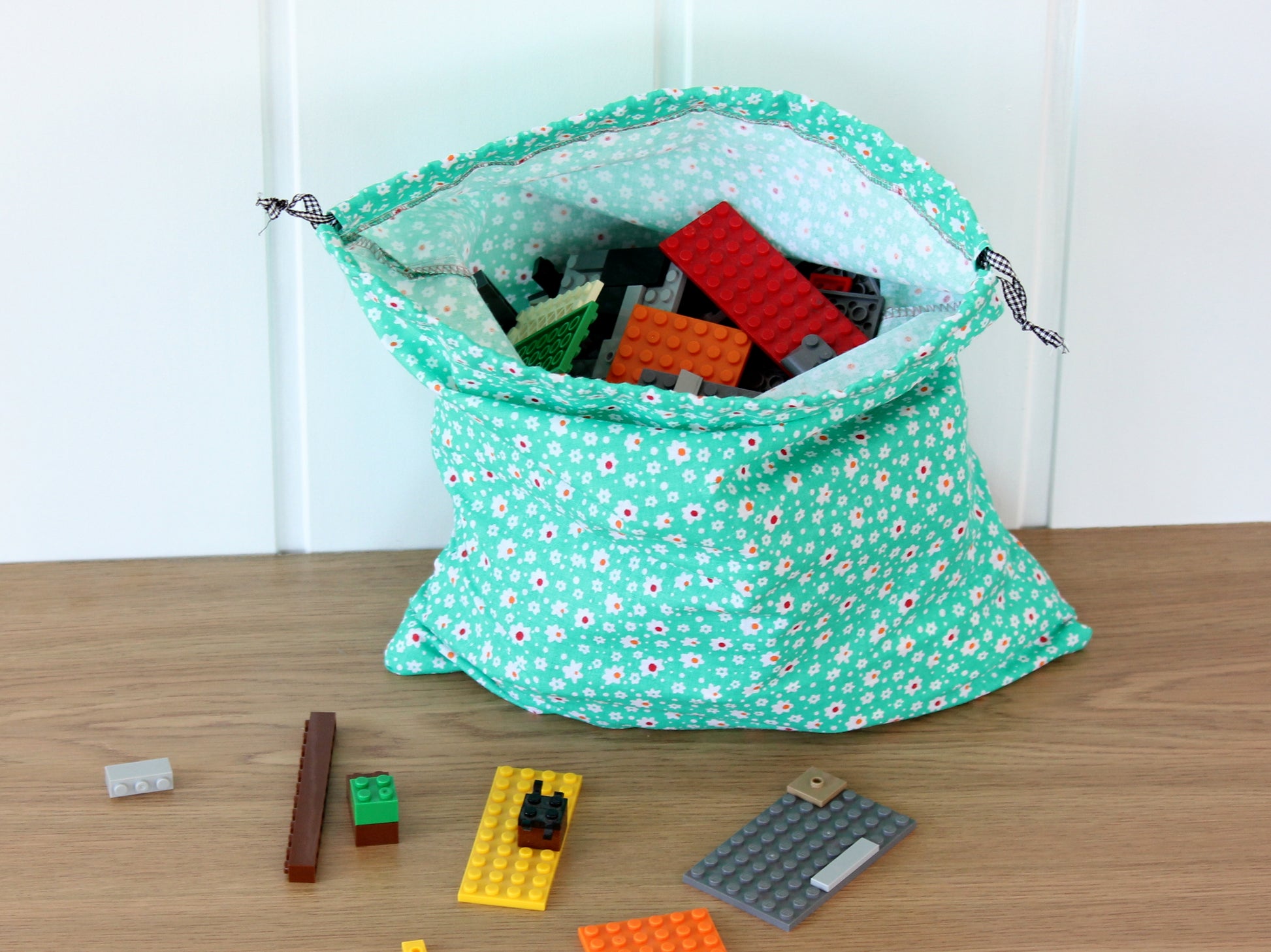 Green drawstring bag with floral pattern containing building blocks on a wooden surface - pattern by NatkoPatterns