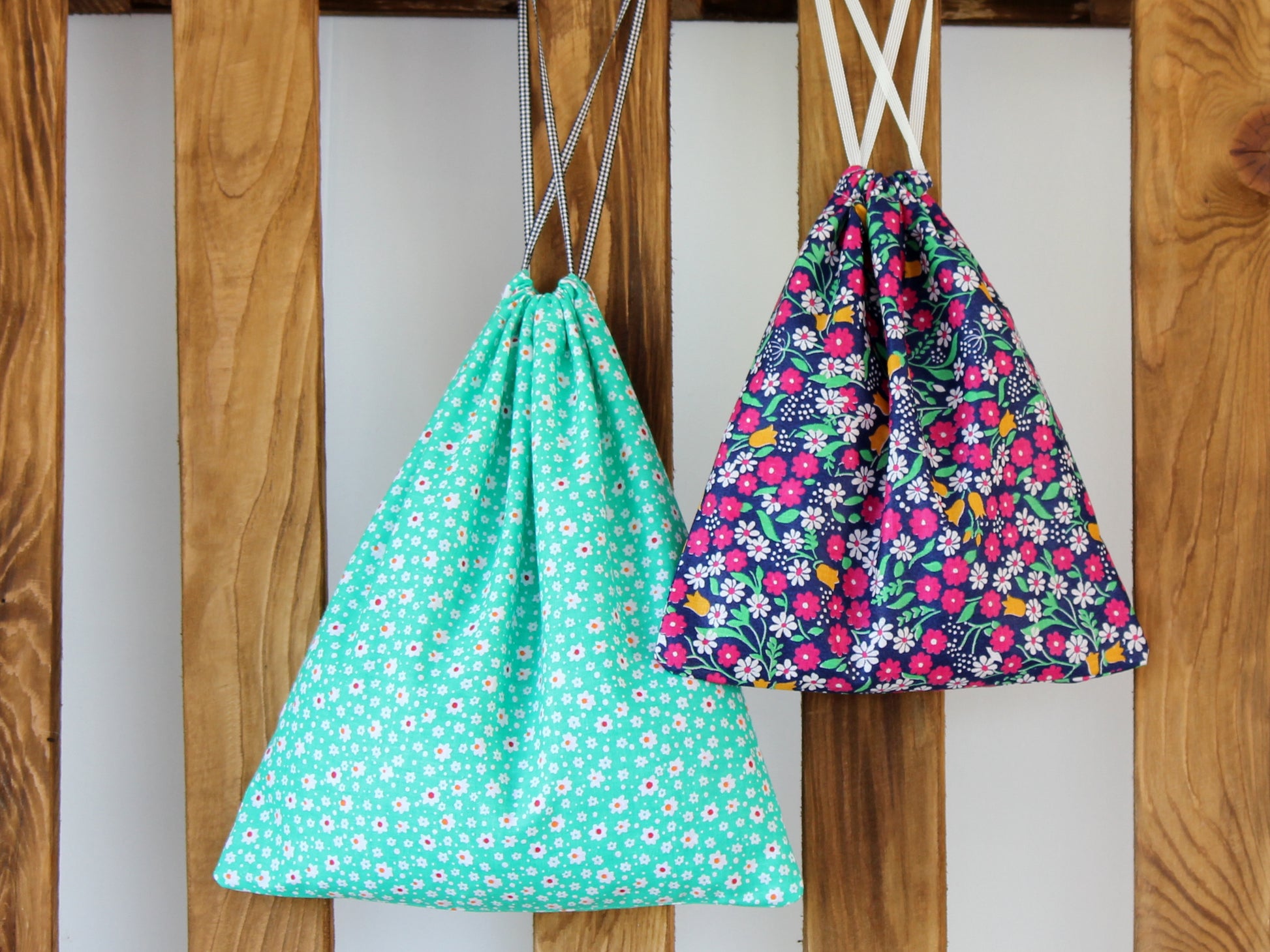 Two floral drawstring bags hanging on a wooden frame - sewing pattern NatkoPatterns