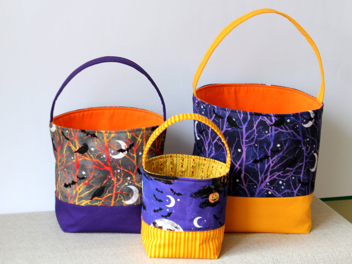 Set of three Halloween trick or treat baskets in different sizes, featuring colorful reversible fabric designs and contrasting handles.