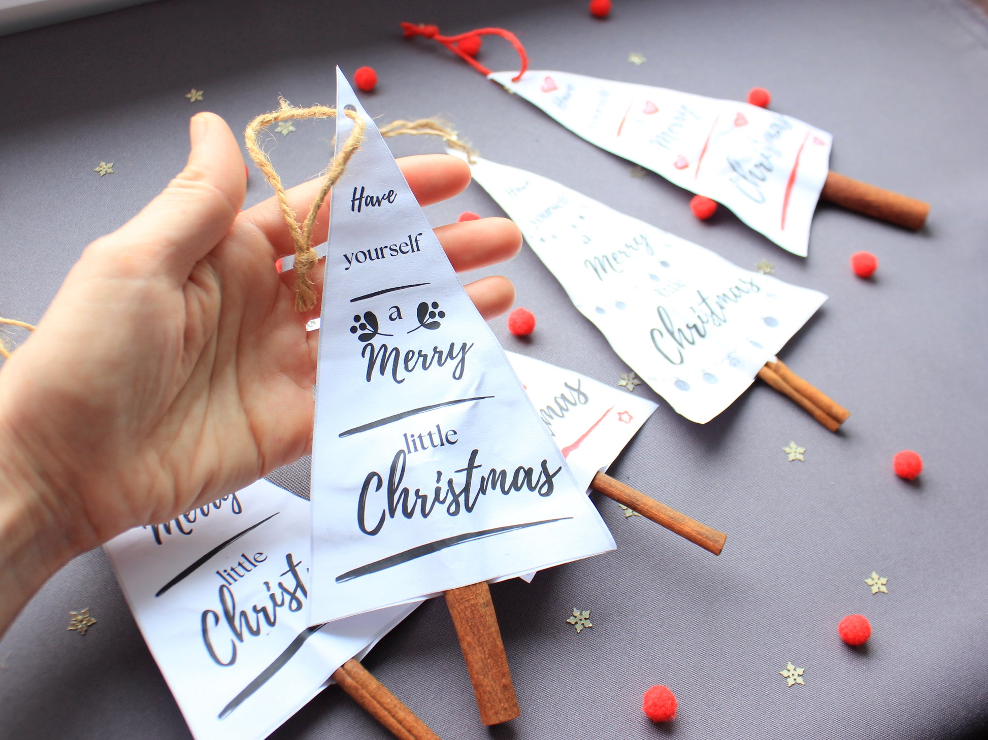 Hand holding a white paper triangle with Christmas text - printable paper decorations for holidays by NatkoPatterns