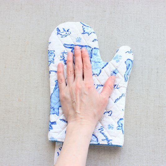 Hand wearing a blue and white patterned oven mitt on a beige surface