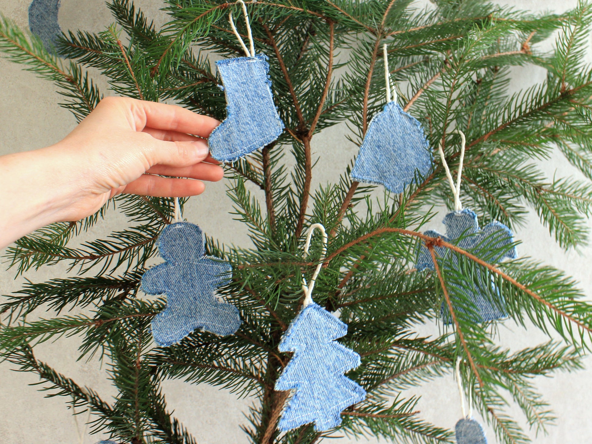 Blue denim Christmas ornament sewn by hand, held on green pine branch, reusable DIY holiday decor