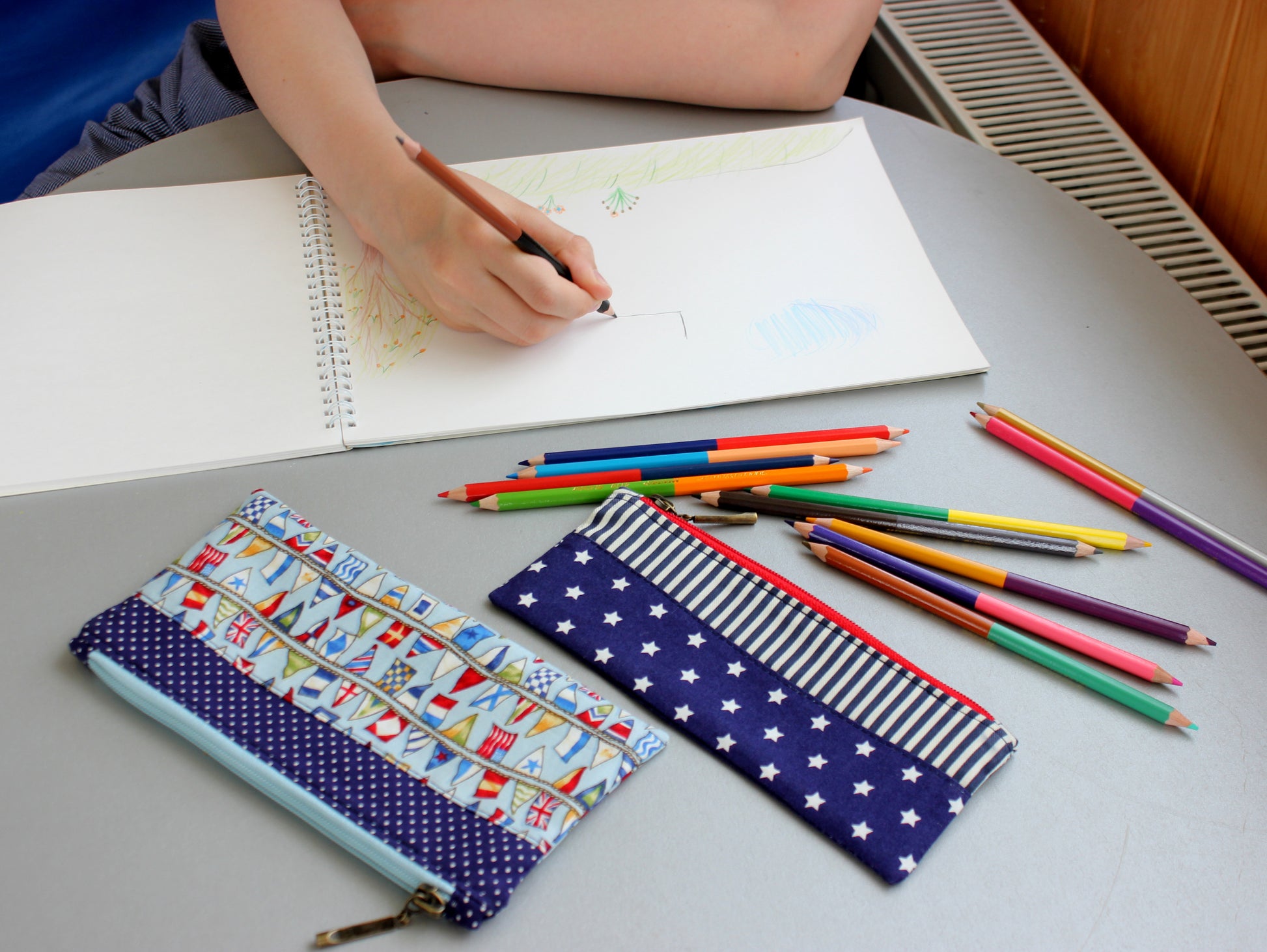 Two fabric pencil cases on a desk with colored pencils around them, indicating a school or study setting by NatkoPatterns