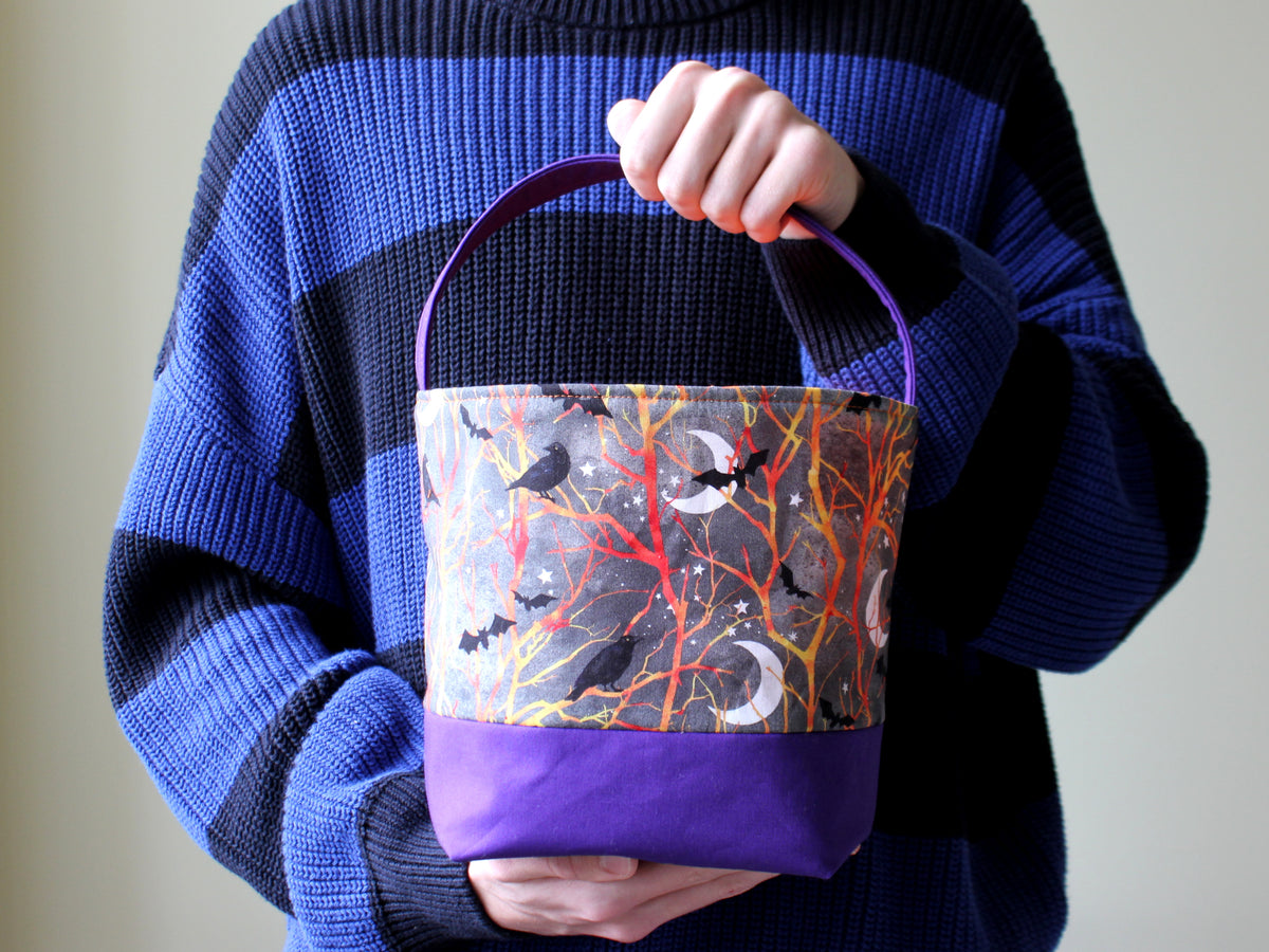 Medium Halloween trick or treat basket held by hand, featuring a purple and blue fabric print, yellow base and matching handle.