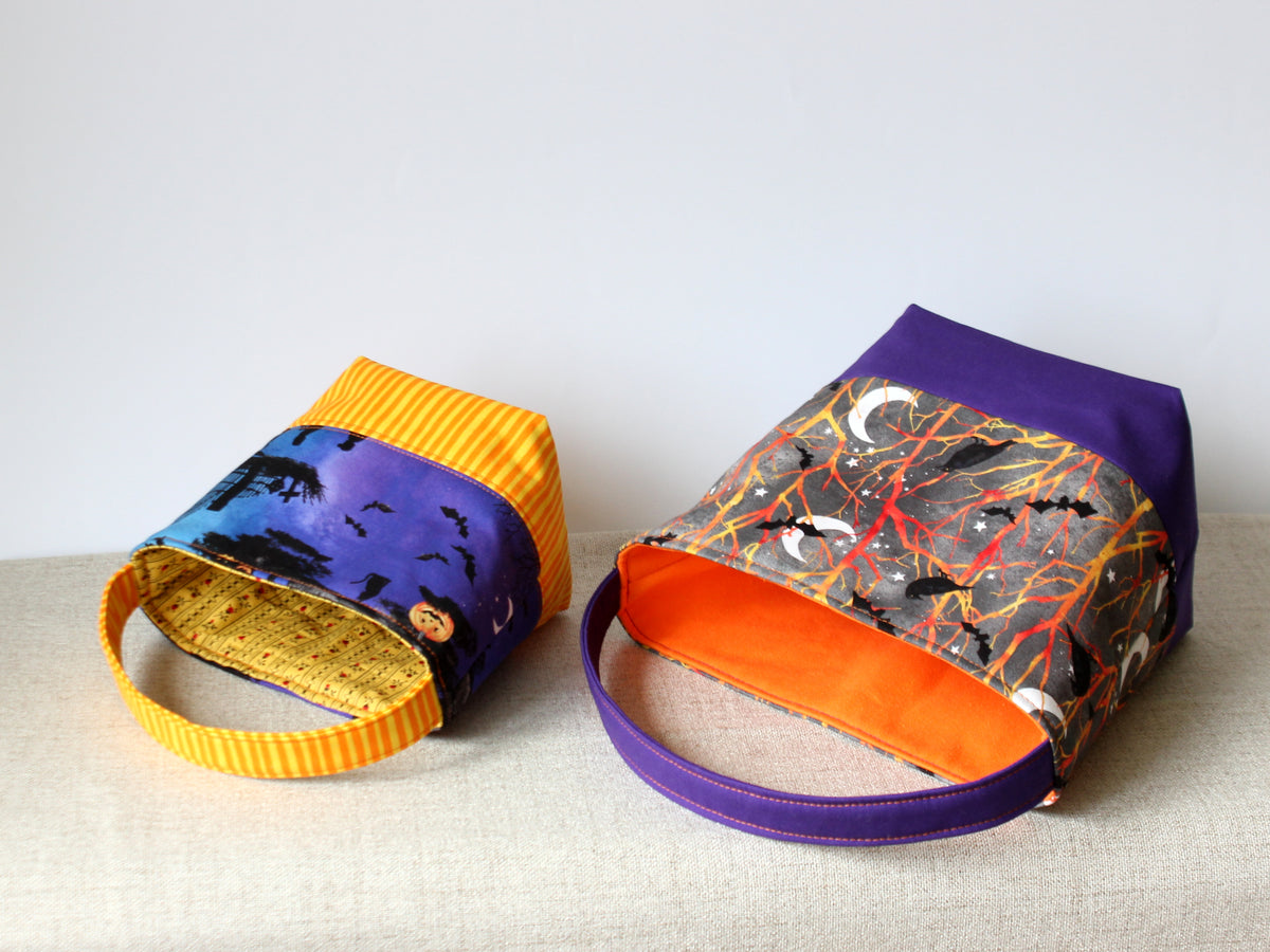 Two reversible Halloween fabric baskets lying on their sides, showing the bottoms and contrasting fabrics.