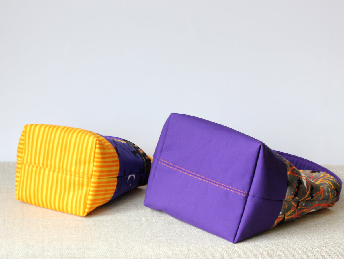 Two reversible Halloween fabric baskets lying on their sides, showing the bottoms and contrasting fabrics.