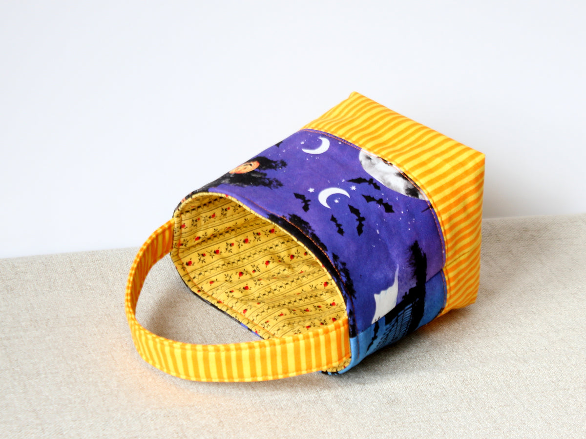 Reversible Halloween fabric basket lying on side, showing the bottoms and contrasting fabrics.