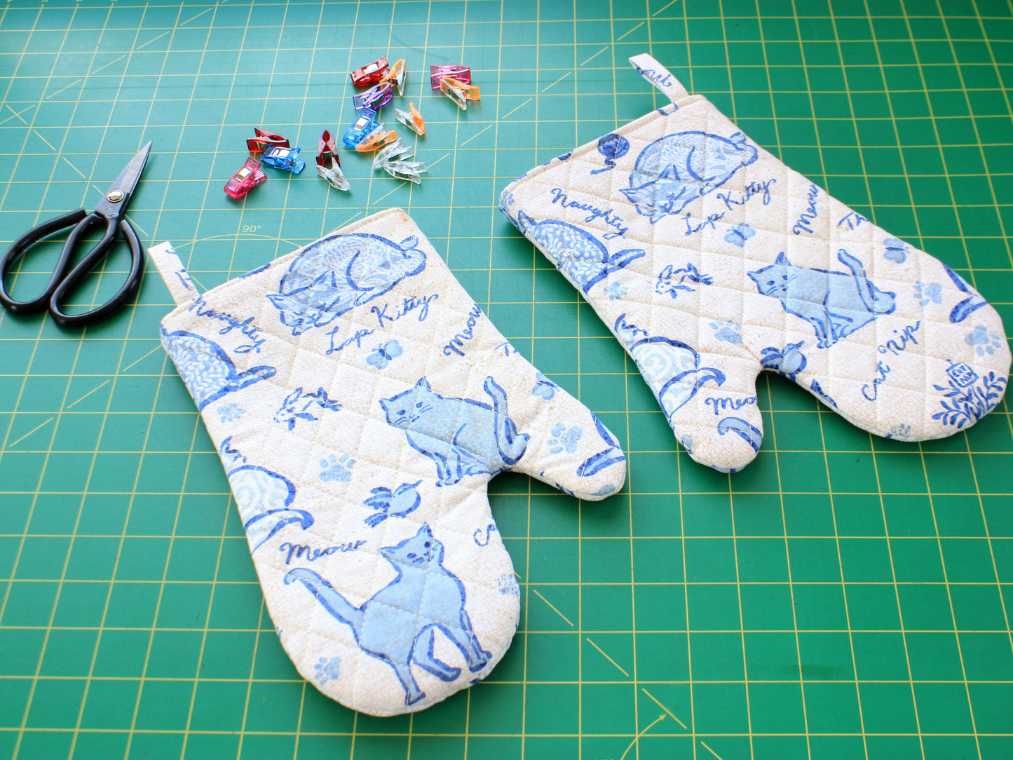 Two handmade quilted oven mitts on sewing table